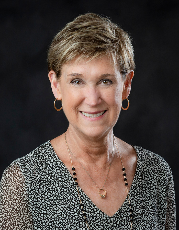 Portrait of Harriet Laird, wearing a dark maroon jacket and white shirt paired with a pearl necklace